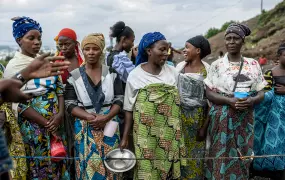 A group of women stand in line. One holds a metal plate.